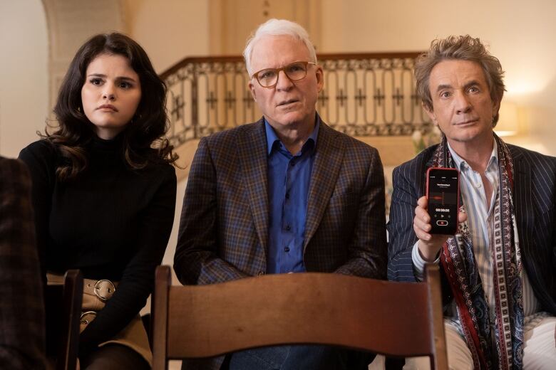 A still frame from the show Only Murders in the Building. Selena Gomez, Steve Martin and Martin Short sit together, looking a combination of concerned and annoyed, as Martin Short holds up an actively recording phone.