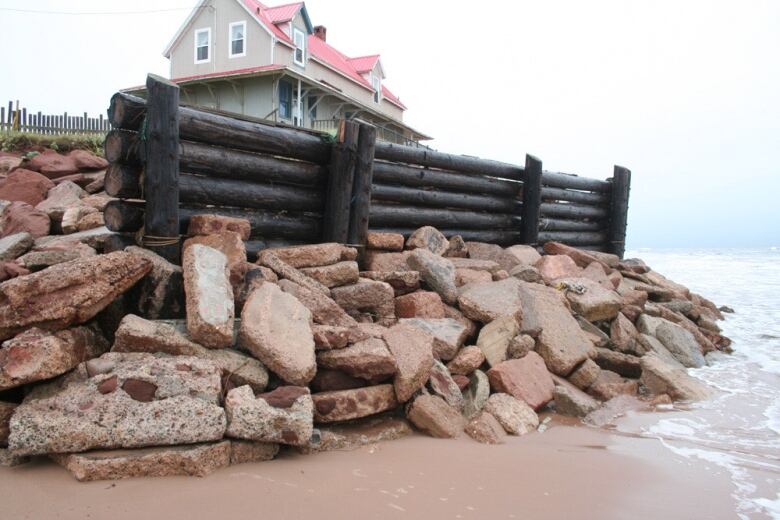 View of a house on top of a hill, with a wooden fence and rock stonewall on a beach.