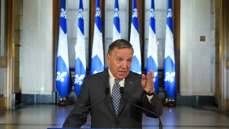 Man in a suit at a podium with one hand raised.