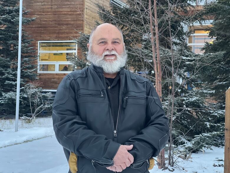 A man with a white beard stands outside in the snow.