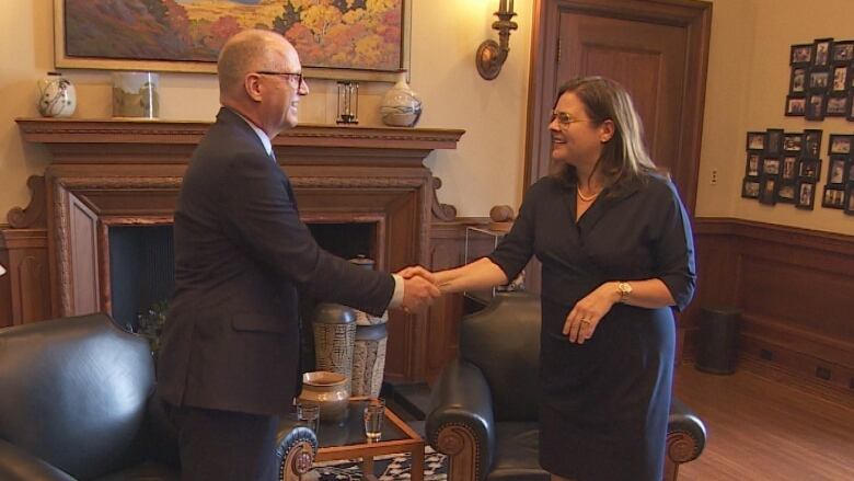 A man in a suit shakes hands with a woman in a dress.