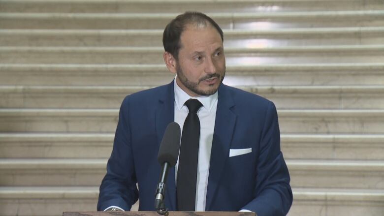 A man in a suit speaks at a podium.