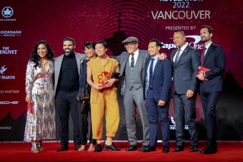 A group of eight people stand on a red-carpeted stage.