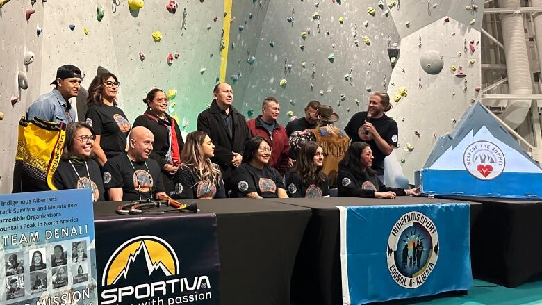 A group of people behind a table. In the background is a climbing wall. 