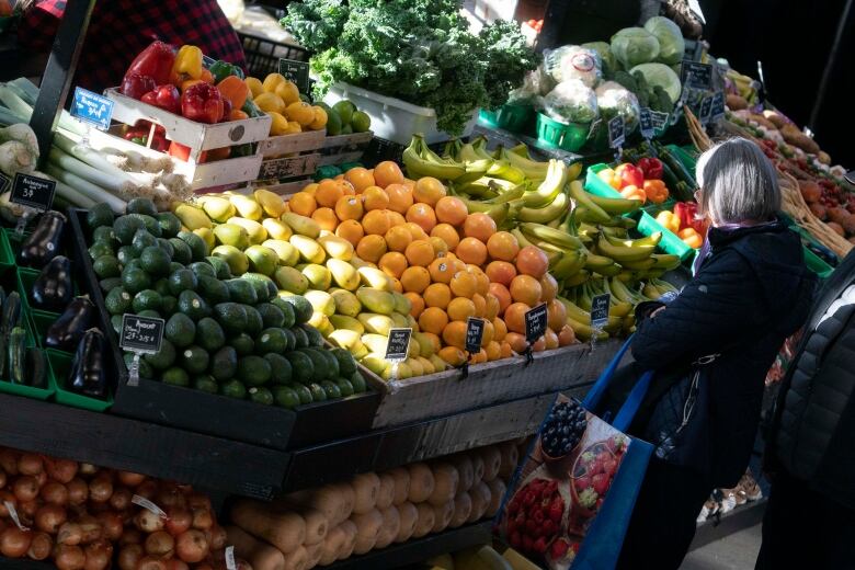 A woman stands in front of a display of oranges and bananas.