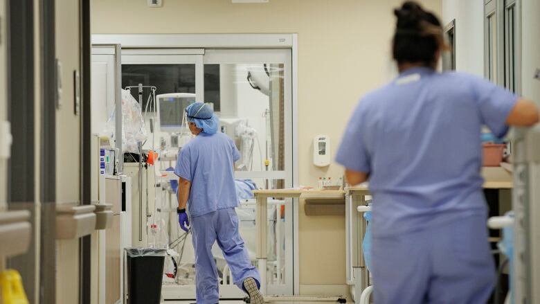 Two health-care workers in blue scrubs are seen in a hospital hallway.