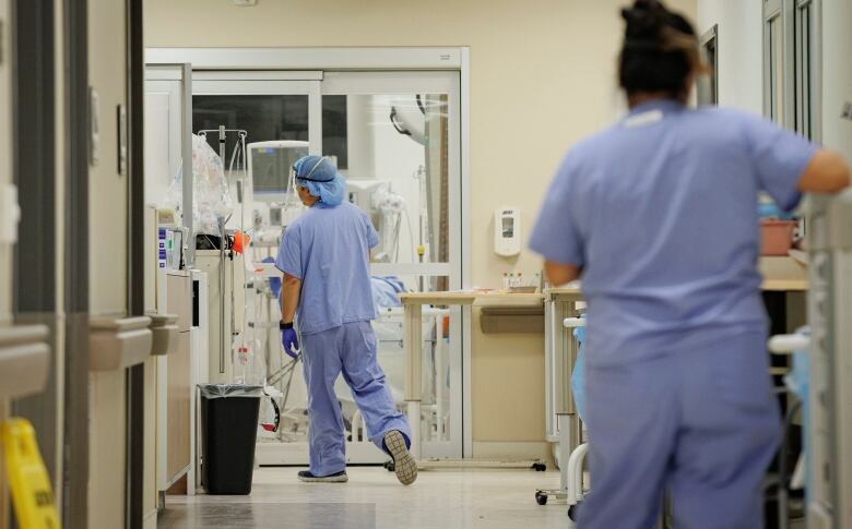 Two health-care workers in blue scrubs are seen in a hospital hallway.