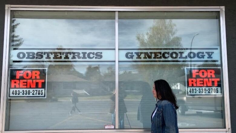 A woman walks in front of the window of an obstetrics clinic. On the window there are two 'for rent' signs