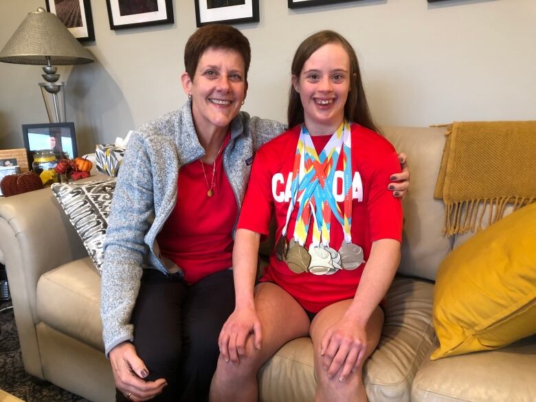 A swimmer wearing swimming medals sitting on a couch beside her mother