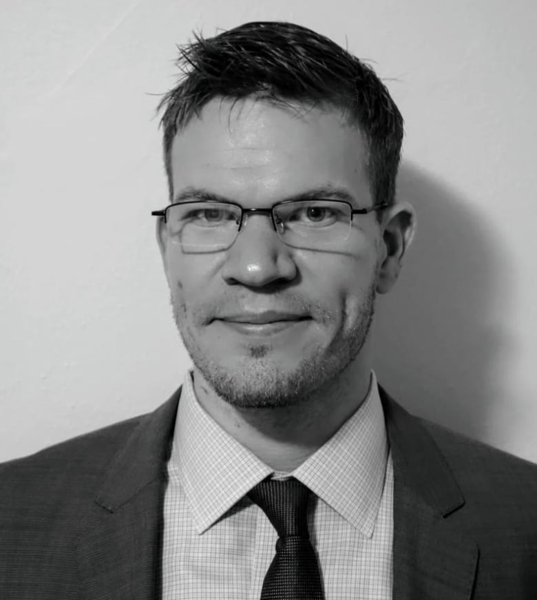 A black and white portrait of a man with glasses wearing a suit.