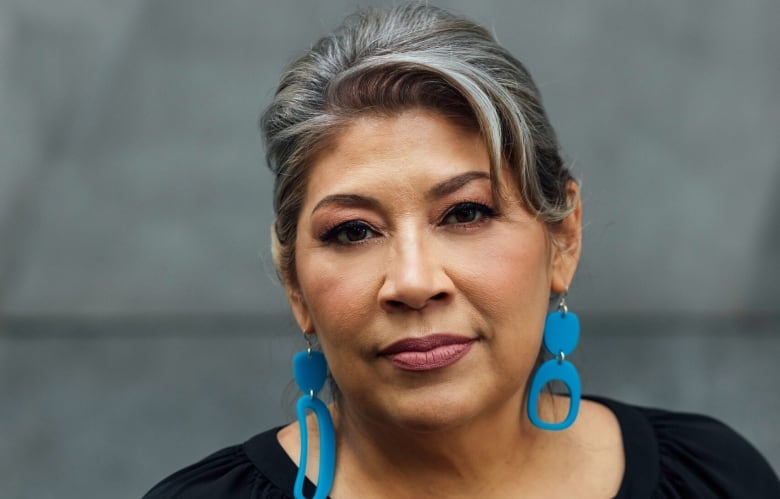 A woman wearing turquoise earrings and a black blouse is pictured looking toward the camera.