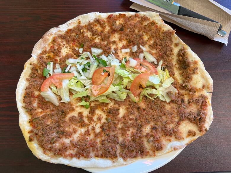 A thin flatbread topped with spiced ground beef, chopped lettuce and tomatoes.