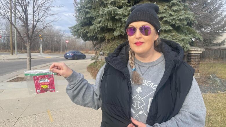 Woman holds up a pink fluorescent package of edible cannabis candy in a ziploc bag.