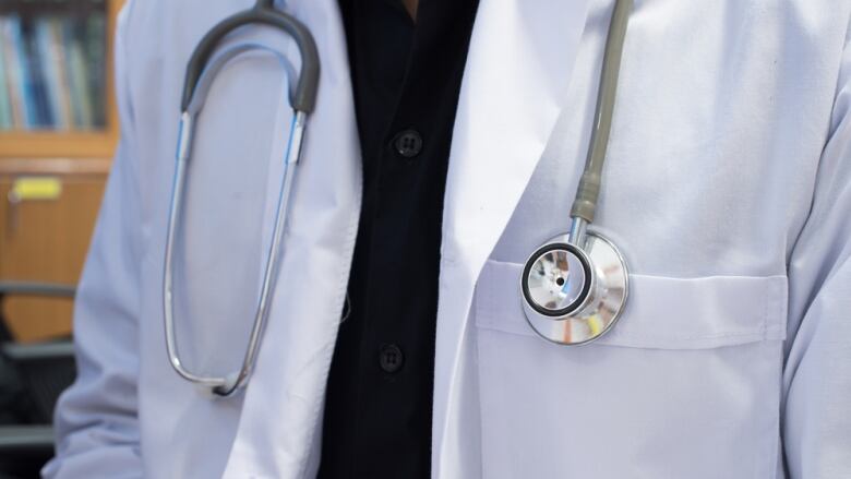 A closeup shows a stethoscope hanging around the neck of a person wearing a white lab coat.