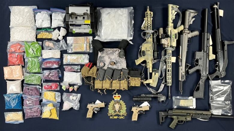 Several baggies containing a variety of suspected drugs in different colours and shapes, laid out beside numerous firearms.