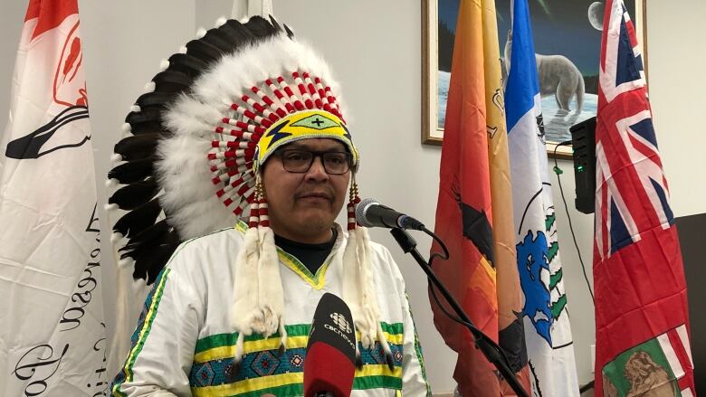 A man wearing an Indigenous war bonnet speaks at a podium.