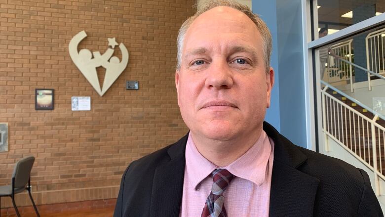 Man stands in front of the public school boards logo.