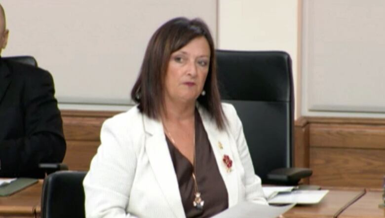 A woman wearing a poppy and white jacket gives a speech