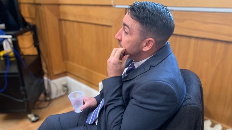 A man in a suit sits on a leather chair in a courtroom