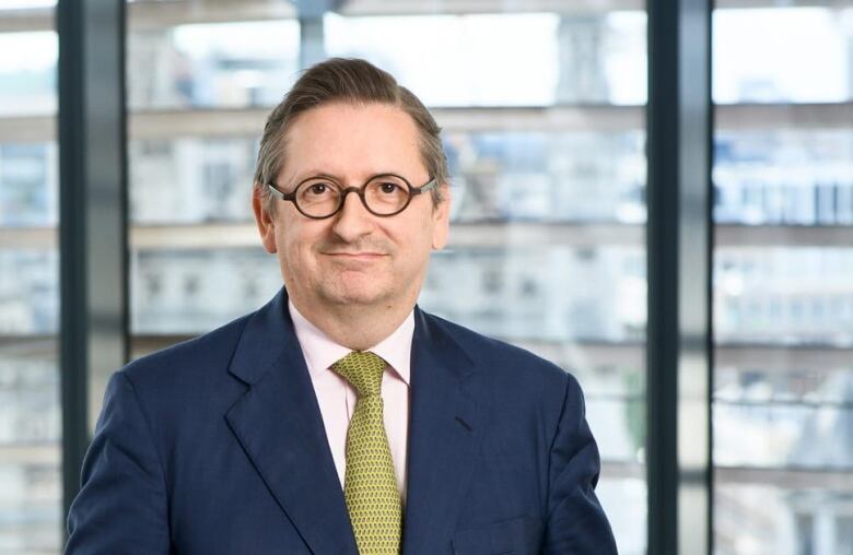 A man is wearing a blue blazer, a green tie and round glasses.  