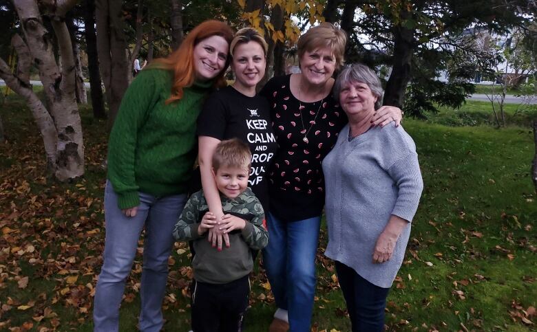 A mother and daughter from Torbay, NL, pose with a grandmother, mother and son from Ukraine. The families have their arms around one another, and are posing in front of a tree on a fall day.