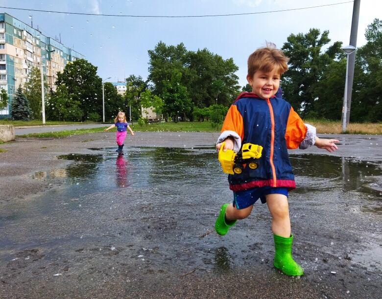 Two young children jump in puddles on a city street in Ukraine.