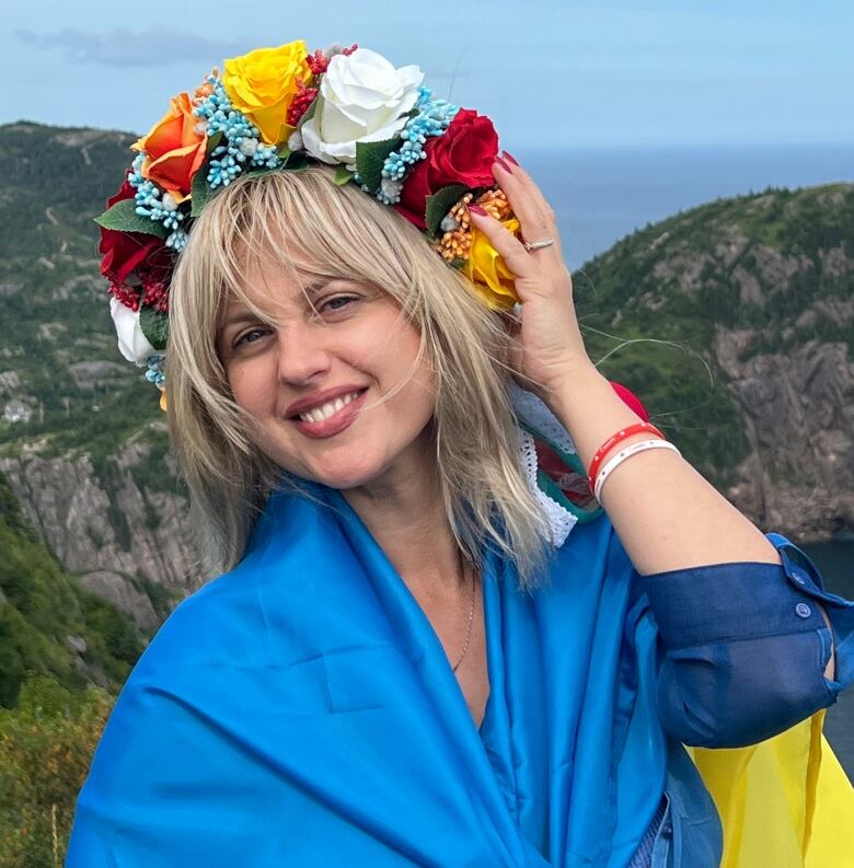 A young woman wears a traditional Ukrainian flower crown and Ukrainian colours as she poses in front of a natural landscape in Newfoundland.