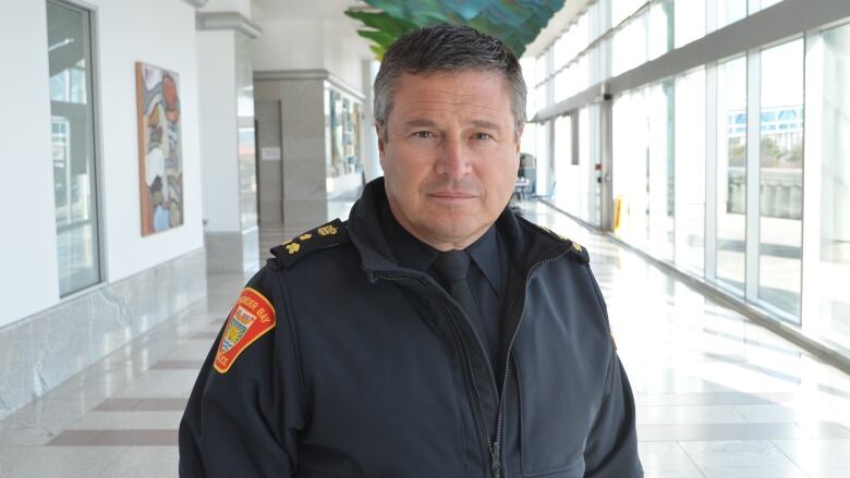 A man standing in a brightly lit hallway looks into the camera.