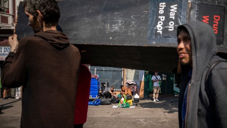 People carry a coffin with the words 'War on the Poor' on it, with people sitting on the pavement in the background.