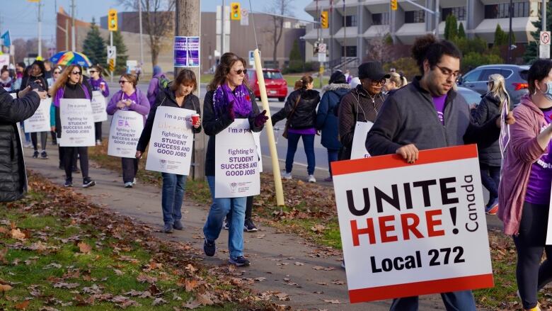 More than a dozen protesters carry signs with education slogans in front of a busy street.