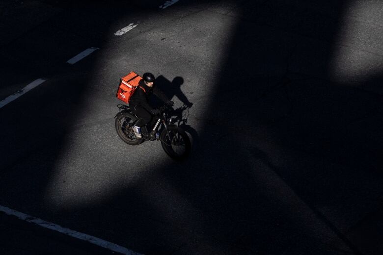 A person atop a food delivery bike is pictured in shadow.