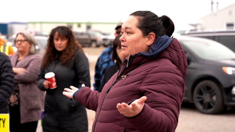 A woman in a purple jacket speaks to a crowd. 