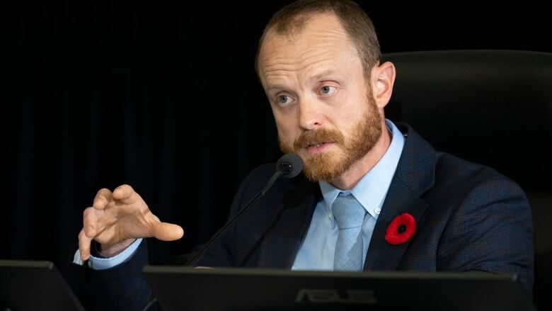 A man with a beard wearing a suit speaking. 