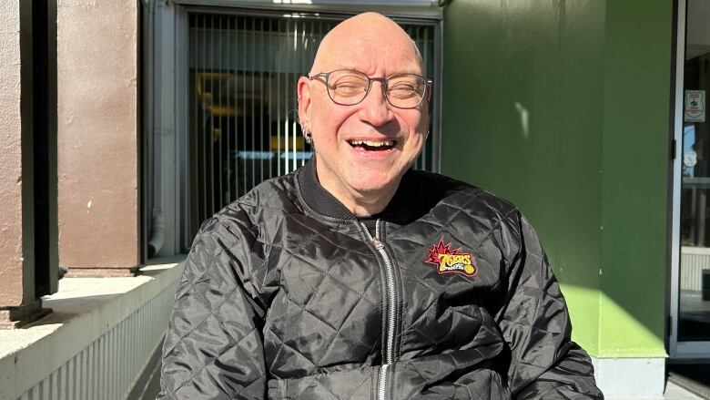 A man with a bald head and multiple piercings in his ears, wearing a black jacket with a logo that says 