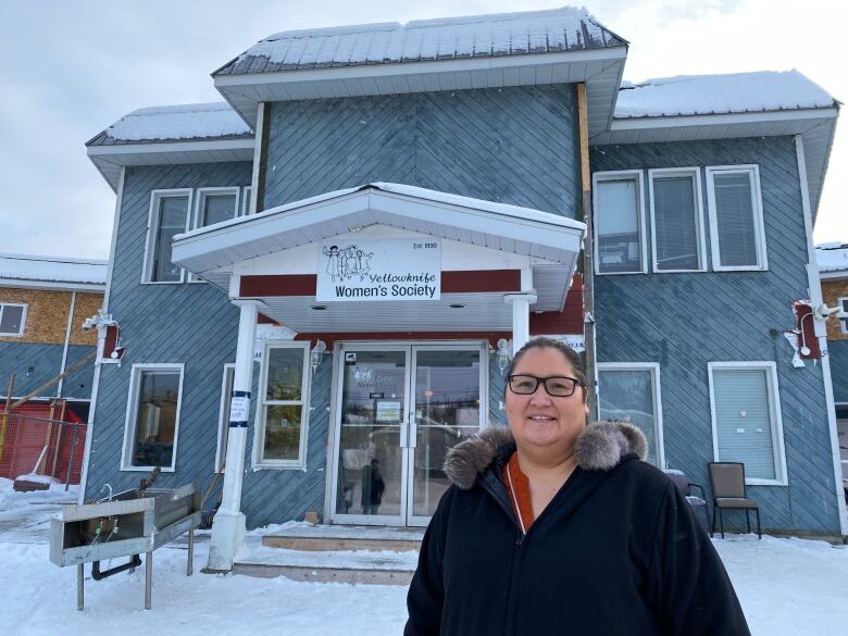 A woman stands outside a building that says Yellowknife Women's Society. 