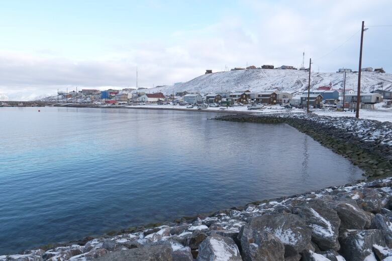 Water, shoreline, buildings sprinkled with snow. 