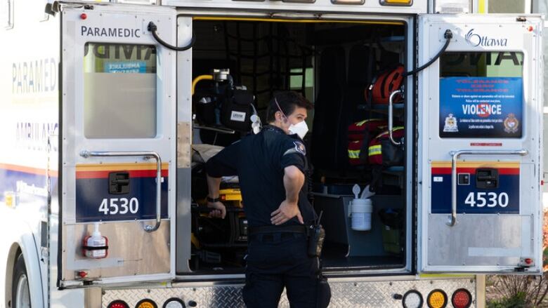 A paramedic in uniform stands behind an open ambulance