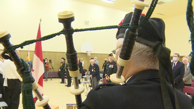 The pipes of a bagpipe frame people who gathered in an auditorium for a ceremony.