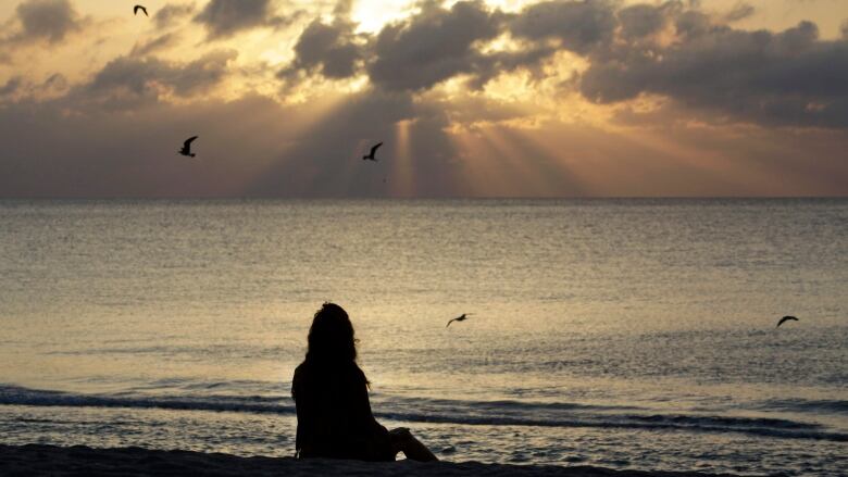 A woman sits on a beach at sunset