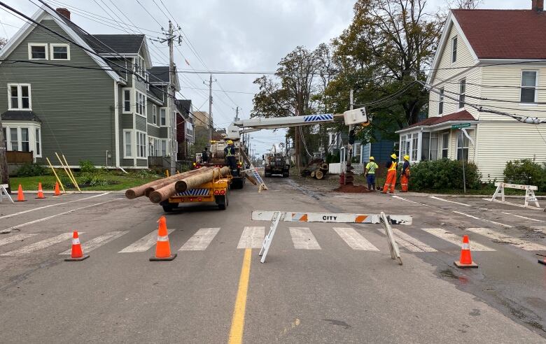 A city street with a flatbed truck and power poles lying on it. Workers stand near the truck. 