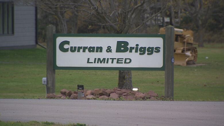 A sign reading Curran and Briggs Limited stands on a lawn with a yellow bulldozer behind it. 