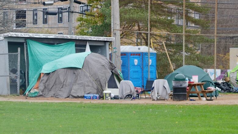 Tents and portapotties site outside the fence of a baseball field, with the dugout visible behind the tarp