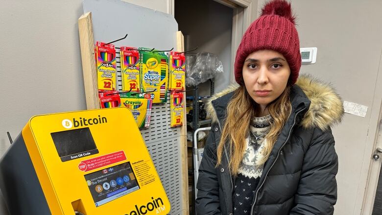 A young frowning woman stands beside a bitcoin ATM.