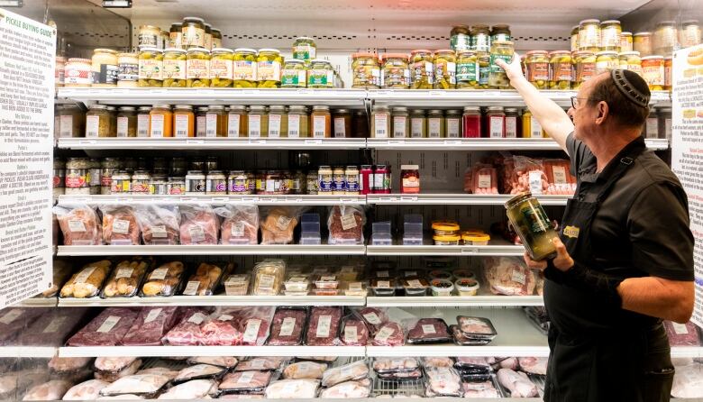 A man with a brimless cap places a jar on a rack.