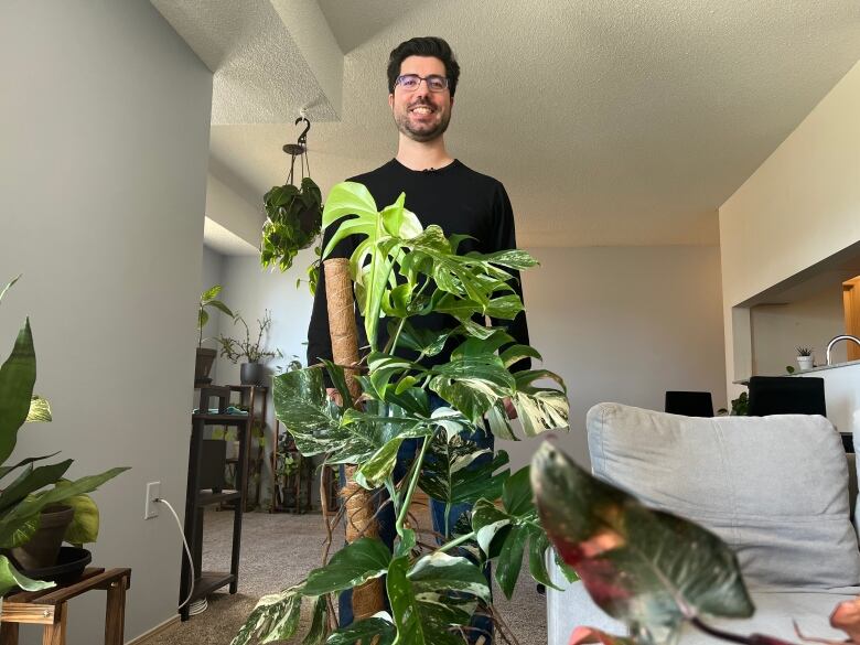 Smiling man stands behind plant.