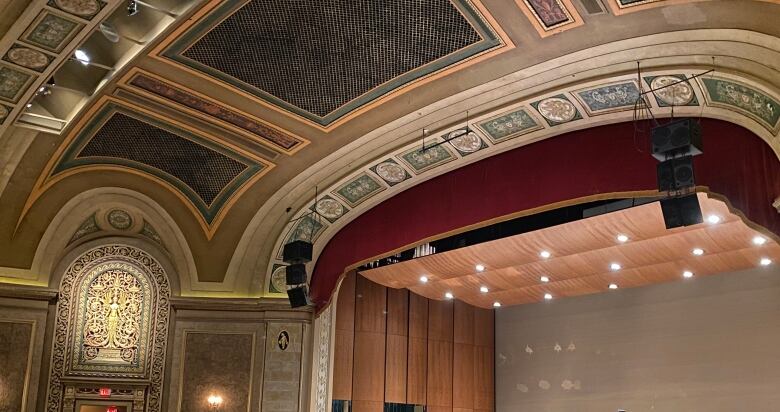 Empty theatre seats and a stage with empty chairs and two men sitting down.