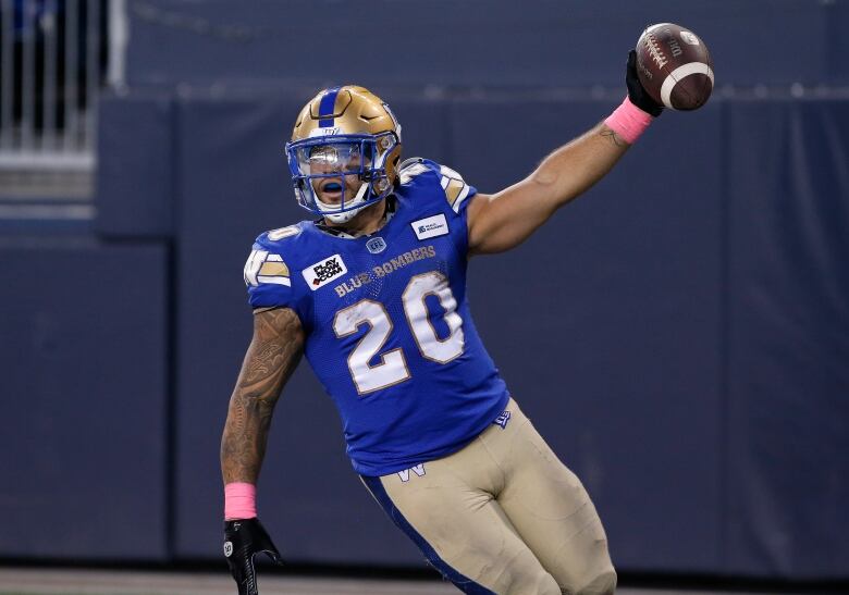 A football player in a blue jersey celebrates by holding a football up in the air.