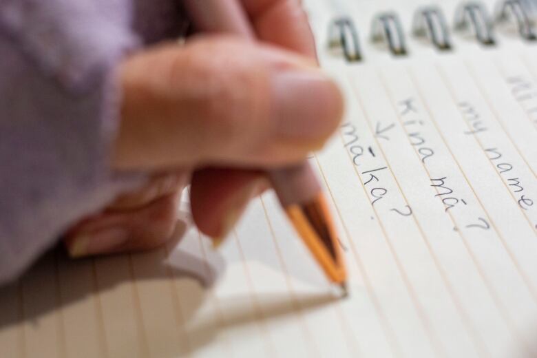 A hand holds a pen writing down words in a note book.