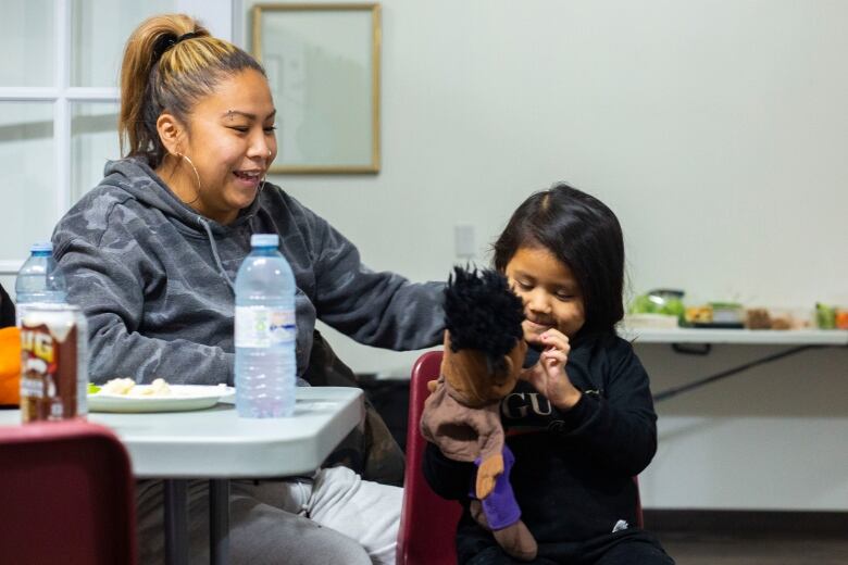 A woman smiles at a little girl playing with a puppet.