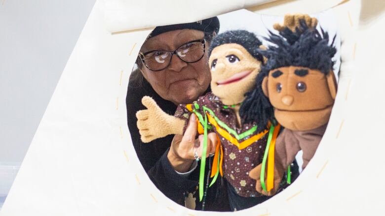 An Indigenous woman acts out puppets talking through a mini-teepee opening.